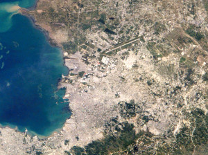 Port-au-Prince aus der Luft: Es sollte nicht vergessen werden, dass durch das verheerende Erdbeben 2010 die arme Bevölkerung des Landes noch mehr geschwächt wurde und der Regierungspalast in seinen Grundfesten beinahe zerstört wurde (NASA, US p.d.).